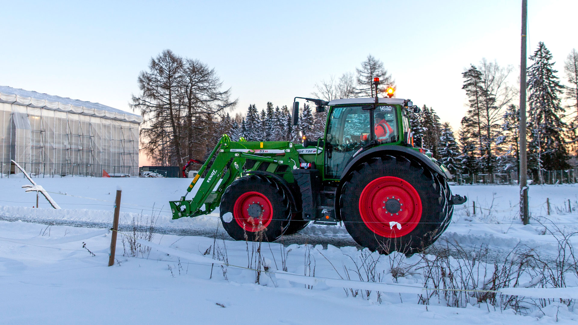 Maatilatyöntekijä työtehtävissään traktorin kanssa lumisessa peltomaisemassa.