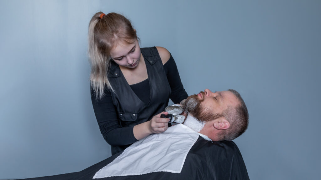 Hius- ja kauneudenhoitoalan perustutkinto, parturi -opiskelija siistii asiakkaan partaa.