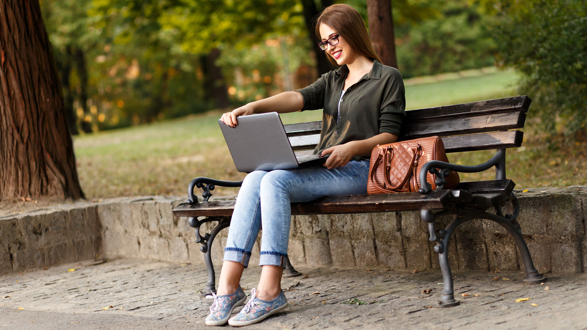 Yrittäjyyden ammattitutkinto-opiskelija, yrittäjä istuu puistonpenkillä tietokone sylissä.