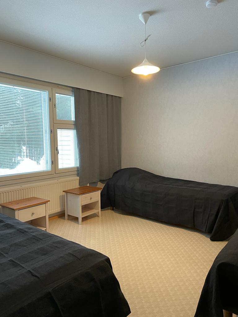 Kuvassa näkymä huoneeseen Hingunniemen hostellissa. Huoneessa kolme sänkyä ja yöpöydät.