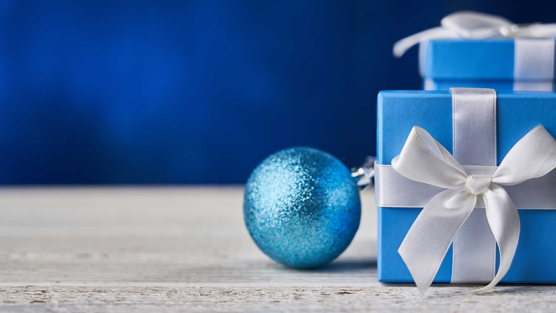 Sininen joulupallo ja kaksi lahjapakettia harmaalla pöydällä.